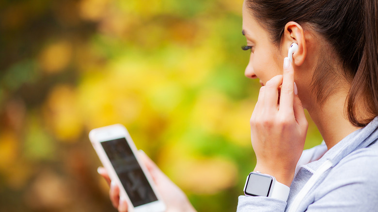 a woman listening to a headphone via Bluetooth and looking at her phone