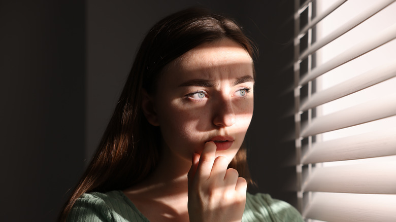Person looking through blinds with a concerned expression
