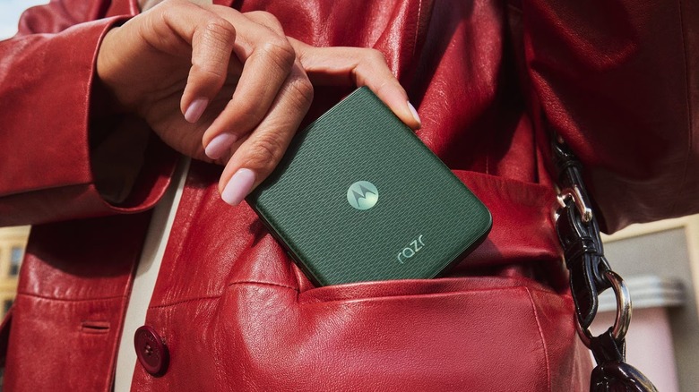 An individual with bright pink nails and a red leather jacket places a black Motorola Razr+ into their jacket's front pocket