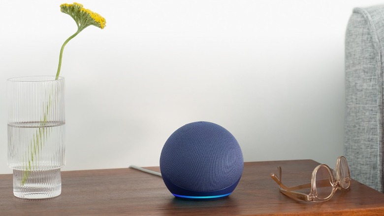 Blue Amazon Echo Dot placed on a wooden table alongside a plant and glasses