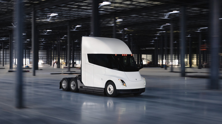 A white Tesla Semi moving through a closed warehouse, front 3/4 view