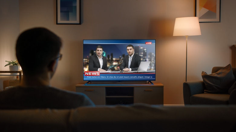 Man watching TV from his couch, with a news program on the screen.