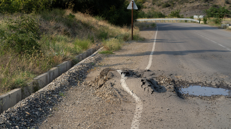 A deformed asphalt surface with potholes caused by heavy trucks and hot summer days.