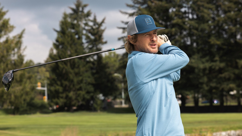 A man wearing a blue shirt and cap swings a golf club