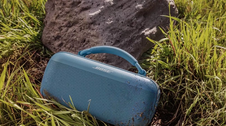 Teal colored Bose soundlink max speaker placed on grass leaning against a rock