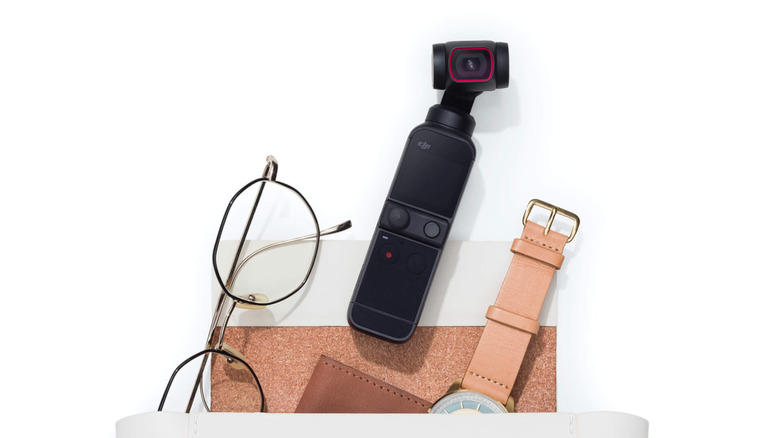 A DJI Pocket 2 camera against a white background near glasses and a watch