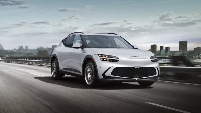 Genesis GV60 driving on a highway with city skyscrapers behind it