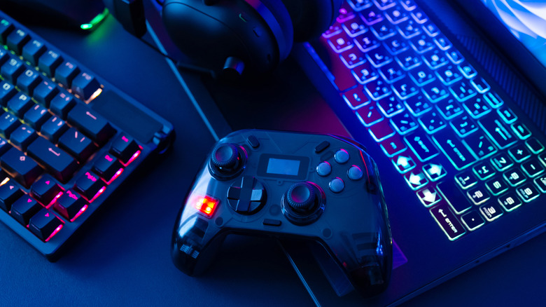 A keyboard, laptop, headset, and controller on a table, bathed in a neon blue light