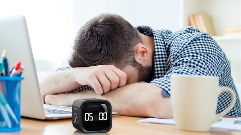 A person taking a nap on their desk, with the Ooraii F4 rotating timer in the foreground.