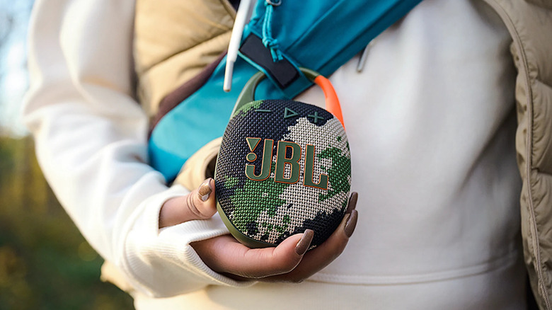 Someone holding a camo-colored JBL Clip 5 bluetooth speaker outside