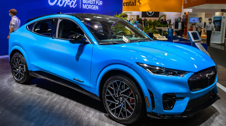 A blue 2022 Ford Mustang Mach-E showcased on the floor of a major car show.