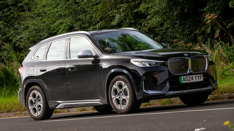 A BA BMW iX driving in front of a forest.