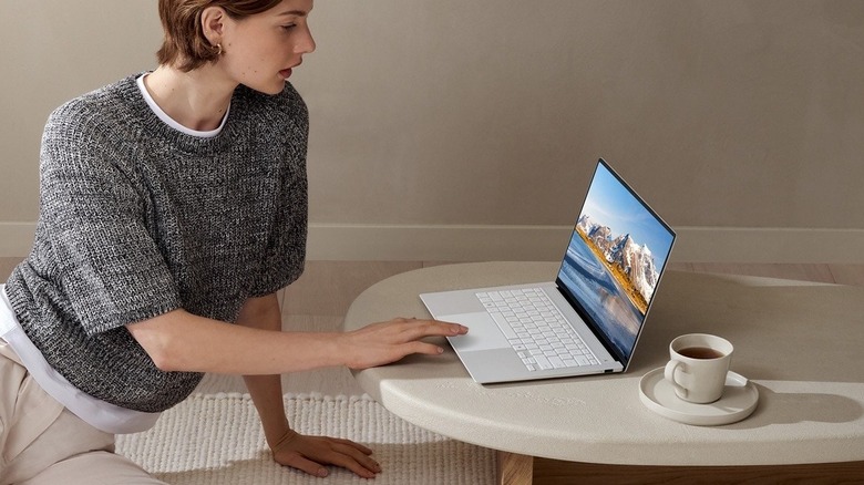 A woman using the Asus Zenbook S 14 on a coffee table.