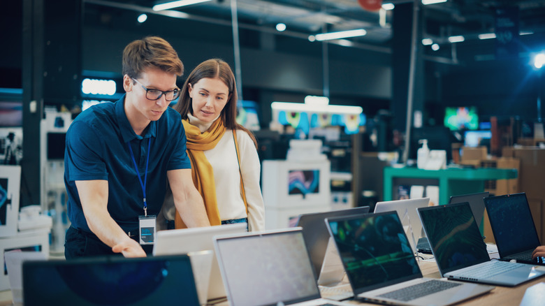 A customer receiving assistance from a salesperson for a laptop in an electronics store.