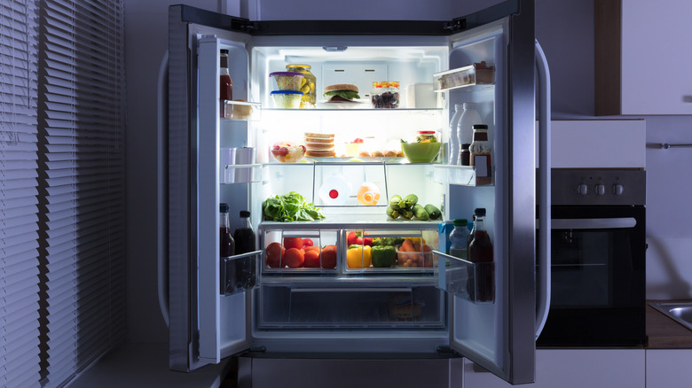 A French-door refrigerator open at night, revealing the illuminated interior and food