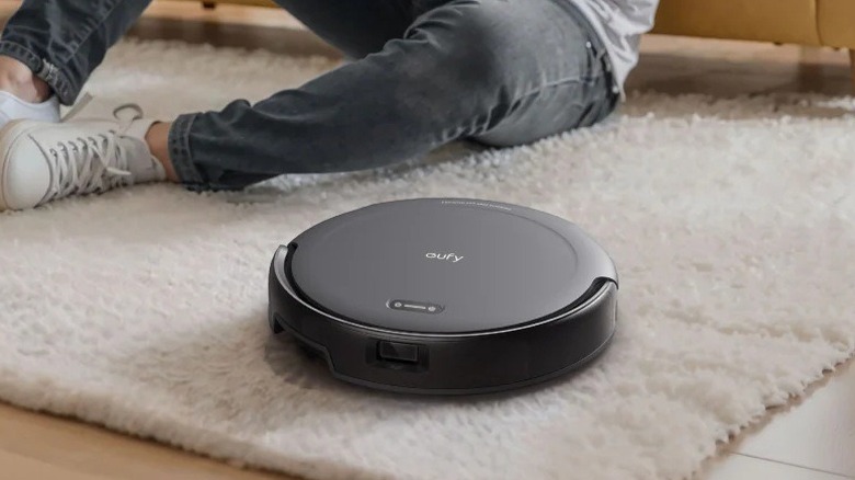 The Eufy C10 T2292 robotic vacuum cleaning a carpet while a person sits nearby.