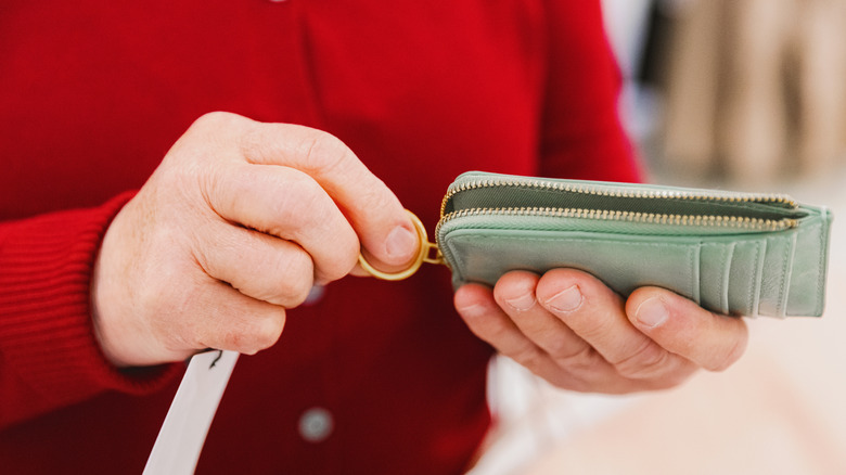 A person in a red sweater opening a green wallet
