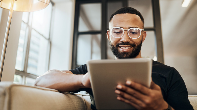 A person wearing specs using their tablet while sitting on a couch