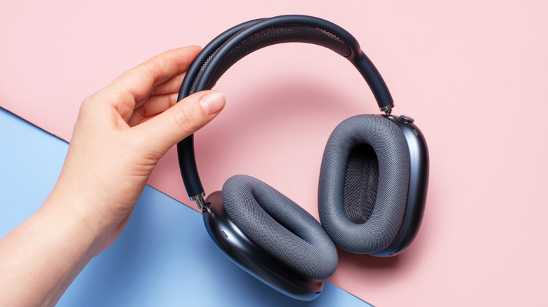A person holding the AirPods Max against a pink and blue background