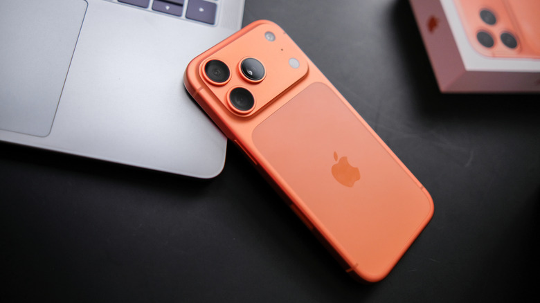 An orange iPhone 17 Pro on top of a Macbook