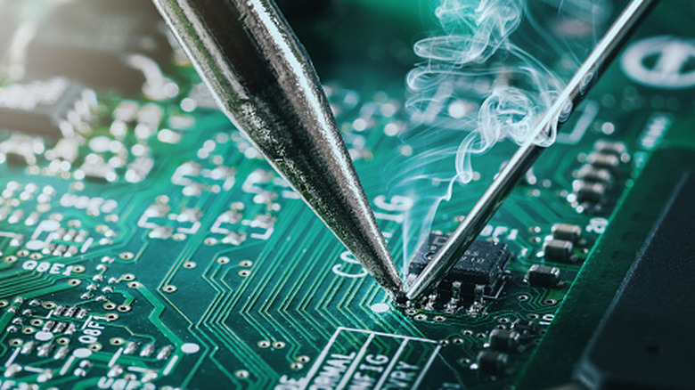 Soldering iron tip soldering component on green PCB