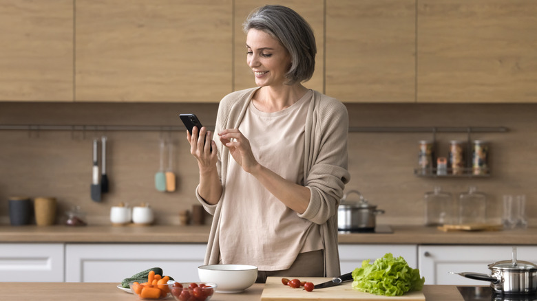 A woman looks at her phone while preparing a salad.