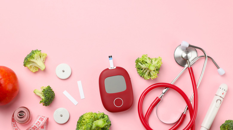 An assortment of fresh foods and diabetes management tools on a pink background.