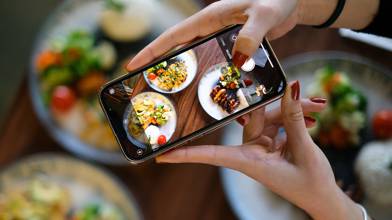 Someone taking a photograph of three plates of food using their smartphone.