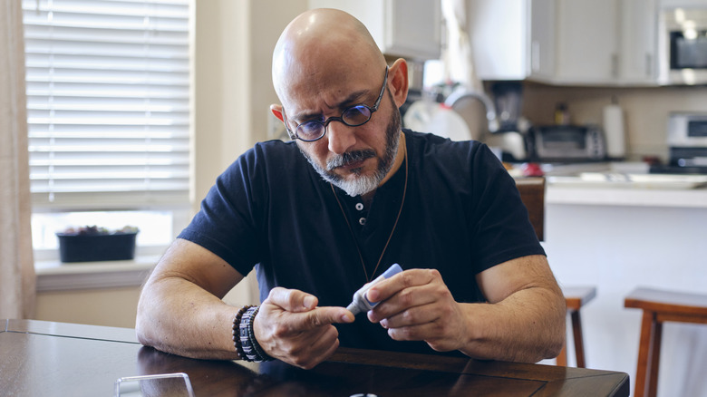 A man sitting at a table and checking his blood glucose levels.