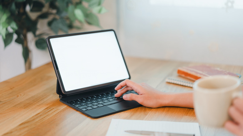 A hand typing on a tablet being used as a laptop computer
