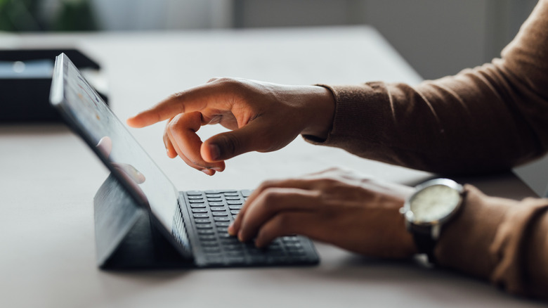 Hands typing on a tablet keyboard, with tablet supported in a case