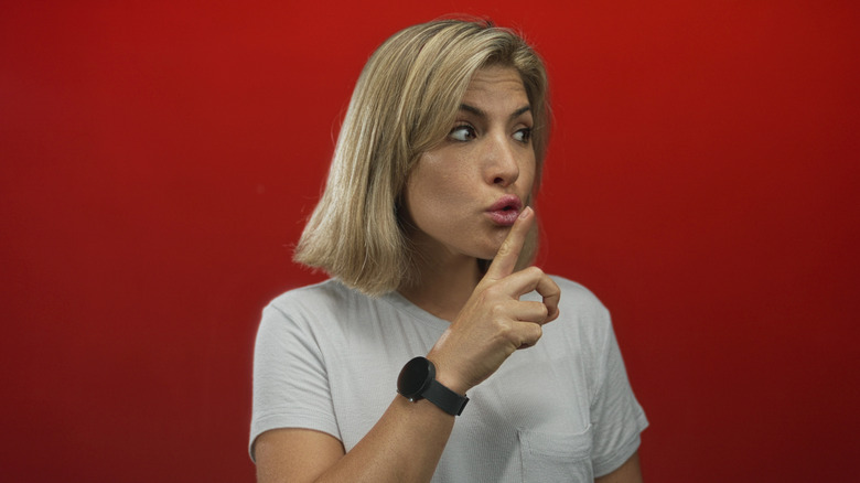 A woman wearing smartwatch and holding a finger to her lips to indicate secrecy