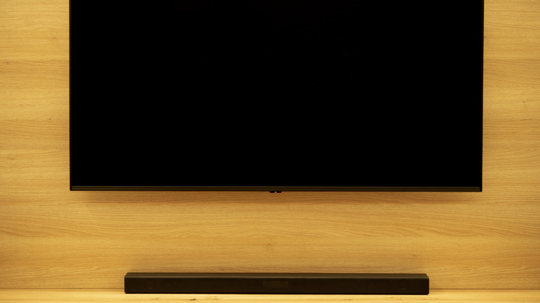 A soundbar sitting on a media stand below a TV