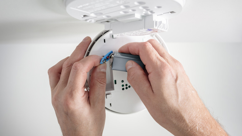 A pair of hands replacing a fire alarm's battery.