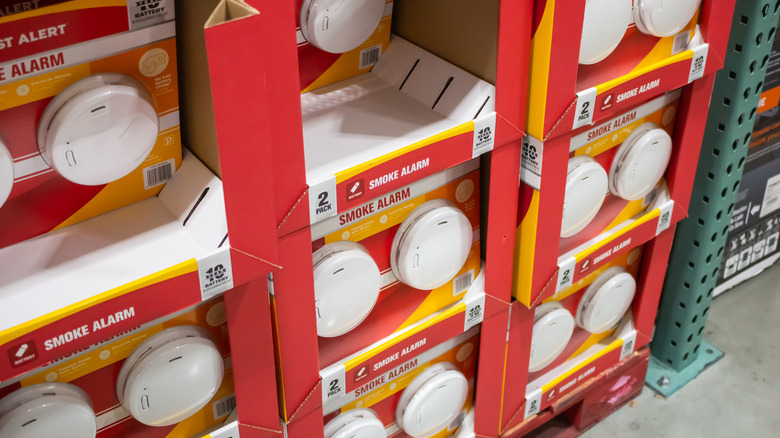 A stack of smoke alarms in cardboard shelving on a shop floor.