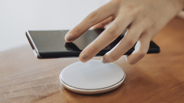 A hand lowering a phone on top of a circular wireless charging pad