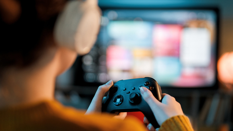 Person with headphones playing on an Xbox Wireless Controller