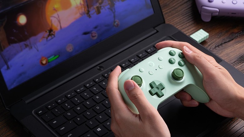 A person using the 8Bitdo Ultimate 2C Wireless Controller to game on a laptop.