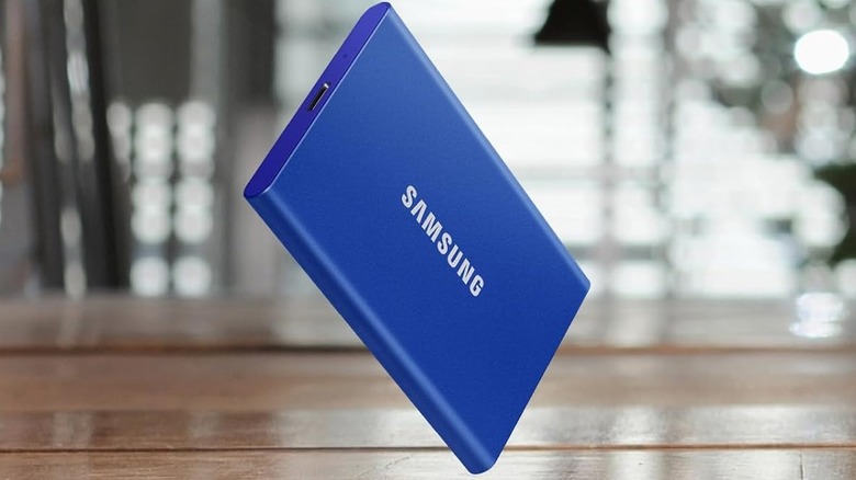 The Samsung T7 1TB Portable SSD (in blue) is about to land on a flat, wooden surface.