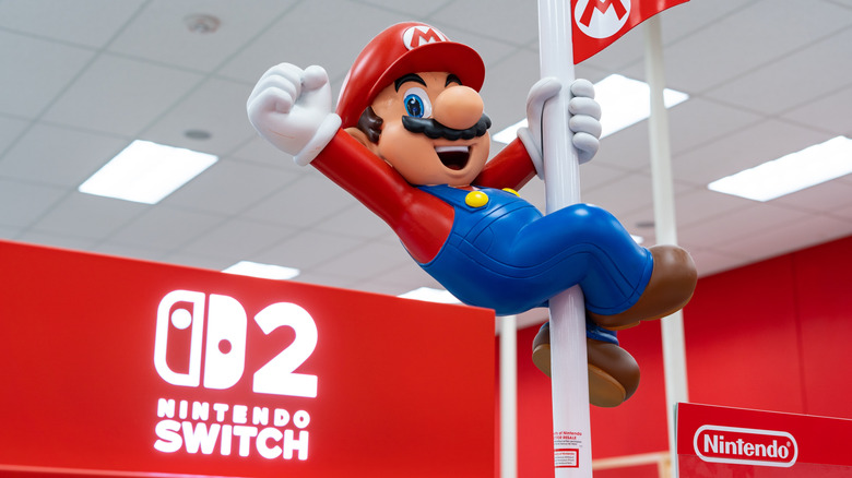 A statue of Mario cheering while holding onto a flag pole. There is a Nintendo Switch 2 logo on a wall behind him.