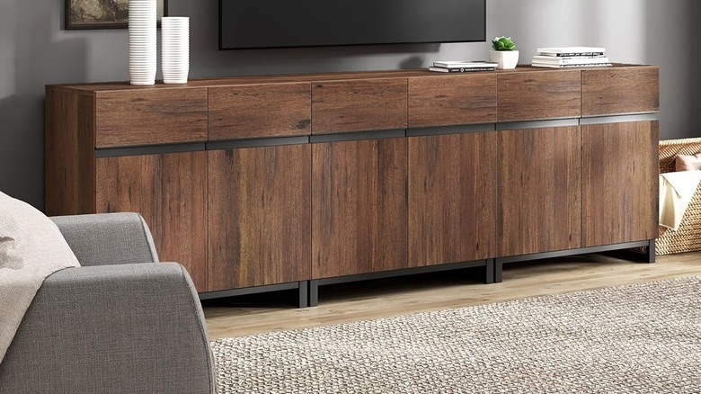 The Wampat Modern TV Stand set up in a living room. A wall-mounted TV hangs several inches above it, and there are books and other items lining the top of the unit.