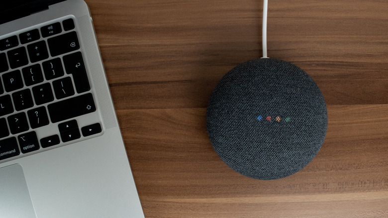 A Google Nest Mini smart speaker on a desk next to a laptop