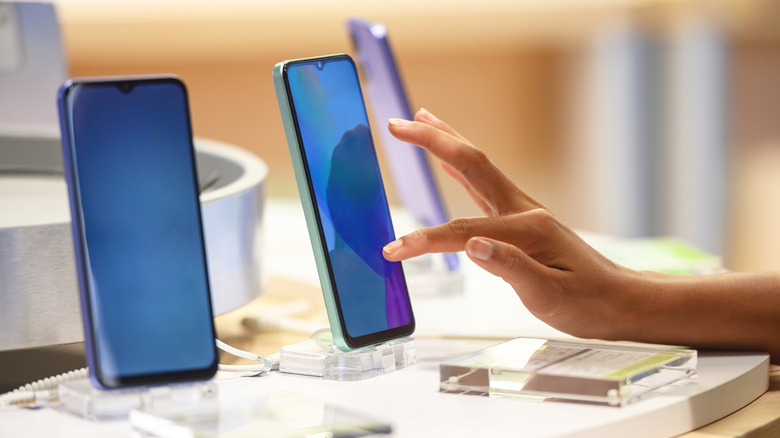 A hand touching a smartphone on display in a retail store.