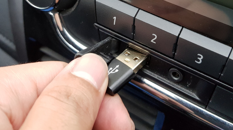 A hand inserting a black USB-A cable into a vehicle's infotainment system