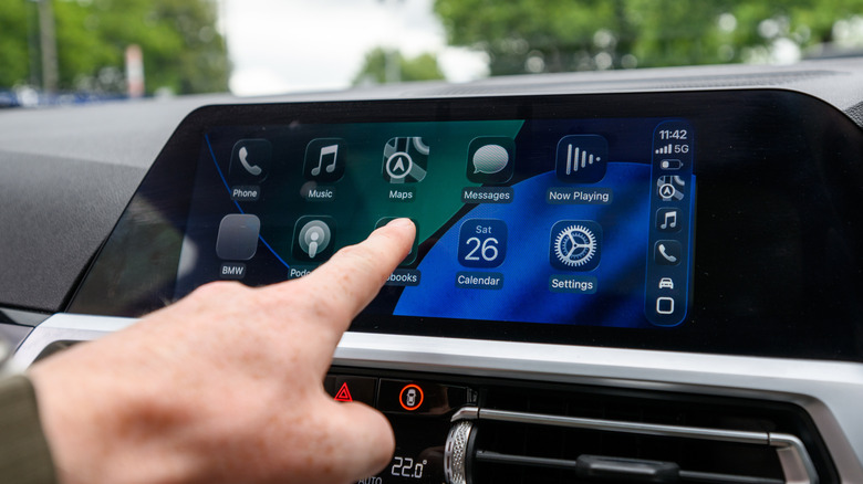 A vehicle infotainment system showing Apple CarPlay with the iOS 26 Liquid Glass theme