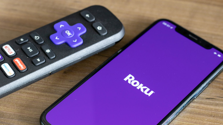 A Roku remote sitting next to a smartphone displaying the Roku logo