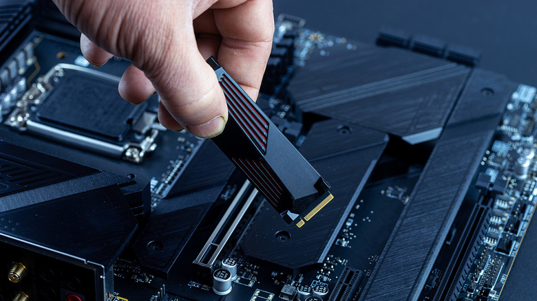 Person installs an M.2 NVMe SSD into a modern motherboard connector, demonstrating the assembly of computer equipment in the process.