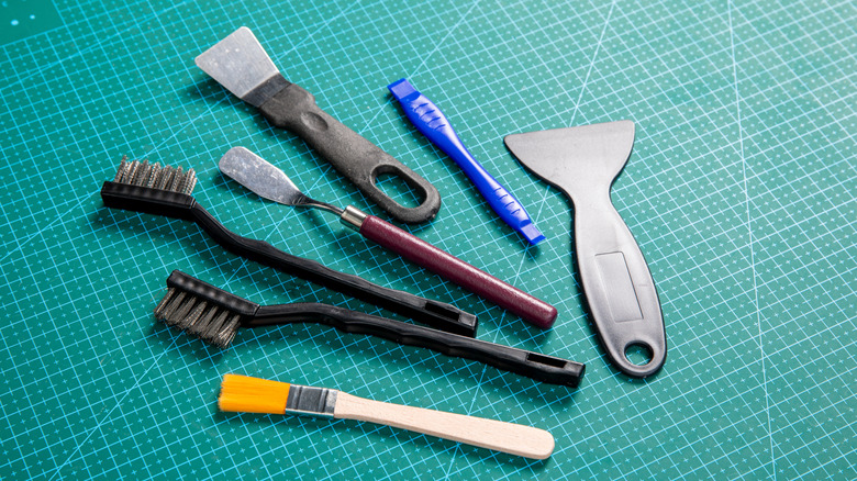 Gray scraper highlighted among 3D printing cleanup tools on a green cutting mat.
