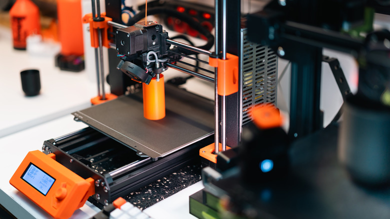 3D printer creating an orange object on its print bed.