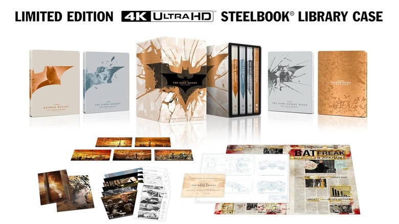 A promotional photo for "The Dark Knight" Trilogy Amazon Exclusive 4K Steelbooks. The image shows each case for the movie, the box it houses all of them in, as well as the extra physical materials that come with the collection.